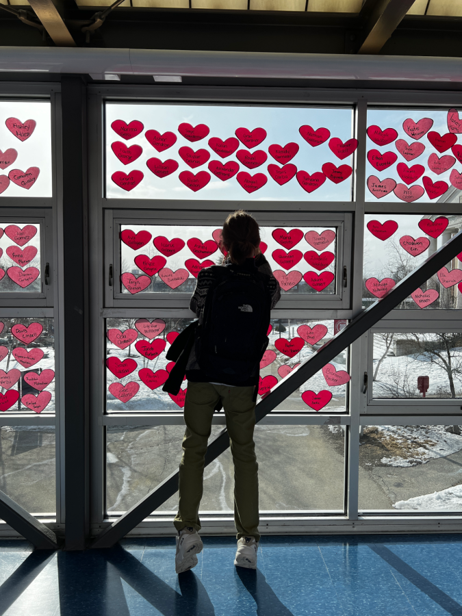 Ayden Blanchard, a Concord High School freshman, writes a message on a friends paper heart taped to the windows of the catwalk on Feb. 14, 2022. 